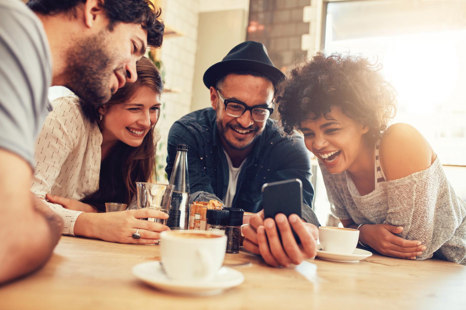 four friends laughing and looking at phone together